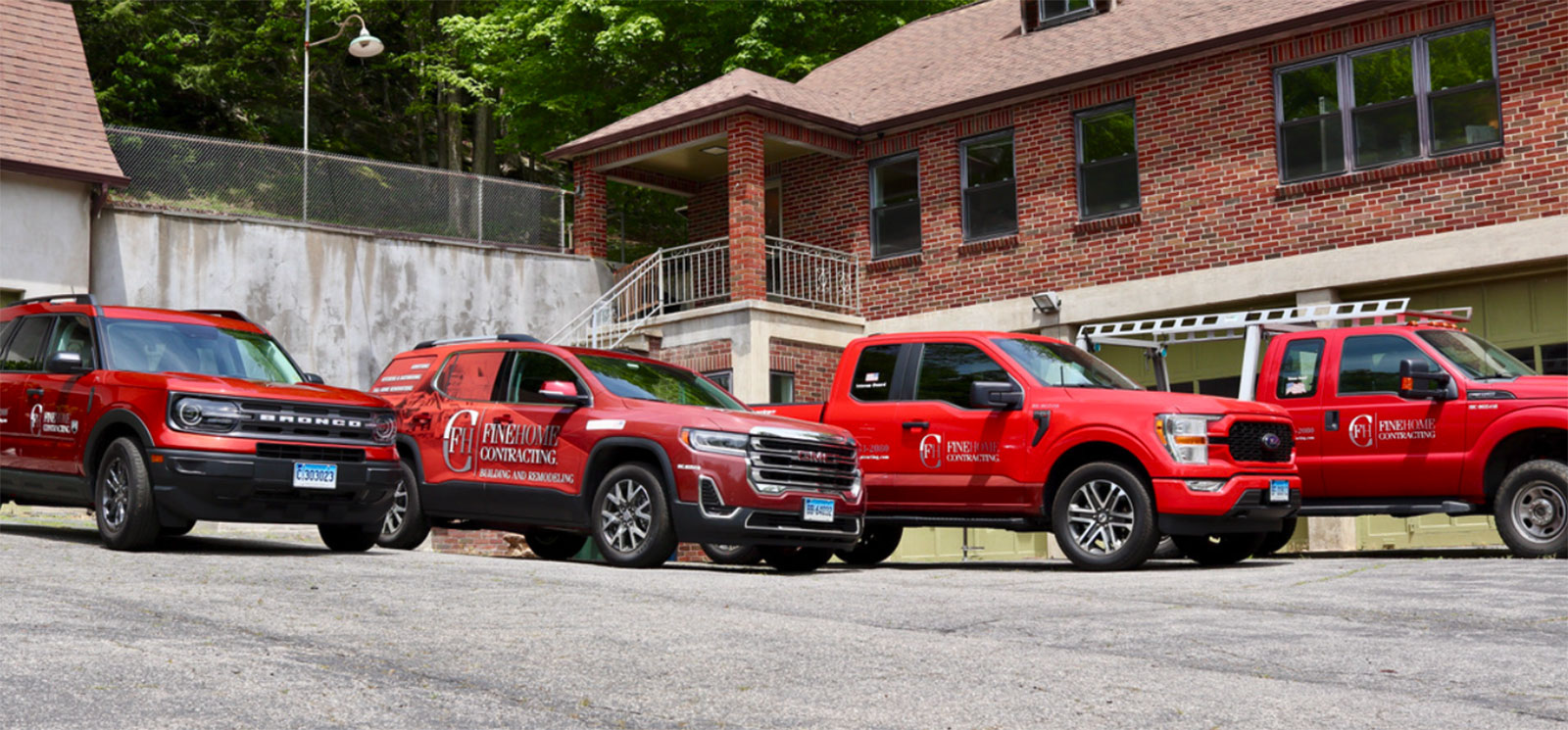 Four red pickup trucks with company branding are parked in front of a brick building on a concrete lot.