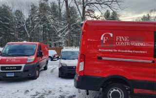 Three red Fine Home Contracting vans are parked on a snowy driveway in a wooded area.