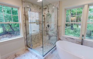 A spacious bathroom featuring a glass shower enclosure, a freestanding bathtub, and large windows offering a woodland view.