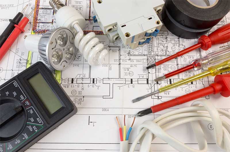 Electrical tools, bulbs, a circuit breaker, and wiring diagram laid out on a technical blueprint.