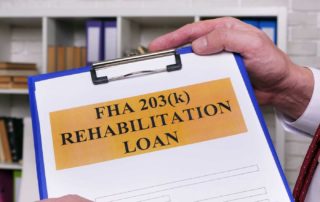 A person holds a clipboard with a document titled "FHA 203(k) Rehabilitation Loan" and blank spaces beneath the heading.