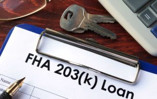 Close-up of a clipboard labeled "FHA 203(k) Loan" with a pair of keys, glasses, and a calculator in the background.