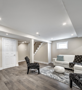 A modern basement lounge area with a white couch, patterned chairs, gray rug, small window, staircase, and white door is perfect for in-law suites.