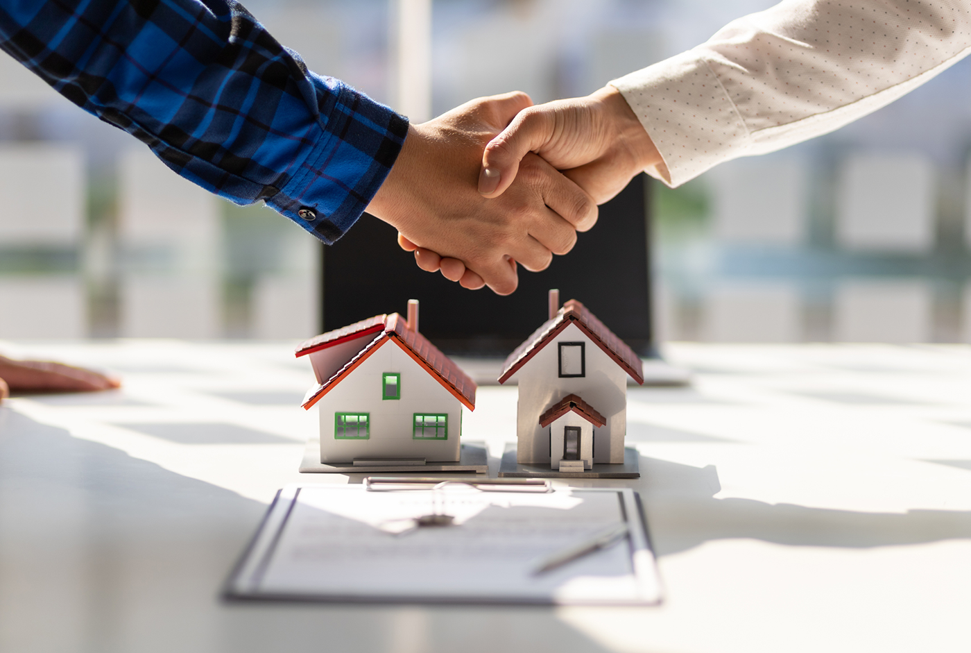 Contractor and homeowner shaking hands over a miniature model house and remodel contract