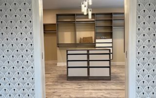 This spacious walk-in closet features built-in shelves, drawers, and hanging rods, all complemented by patterned wallpaper and wooden flooring.