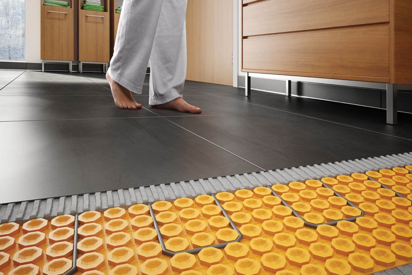 Person walking barefoot on a tiled floor with a view of partially installed orange floor heating system.