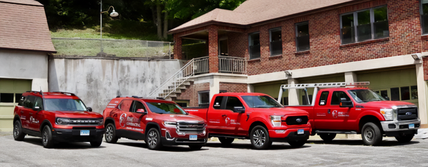 Four red utility vehicles are parked in front of a brick building with a garage and an exterior staircase.