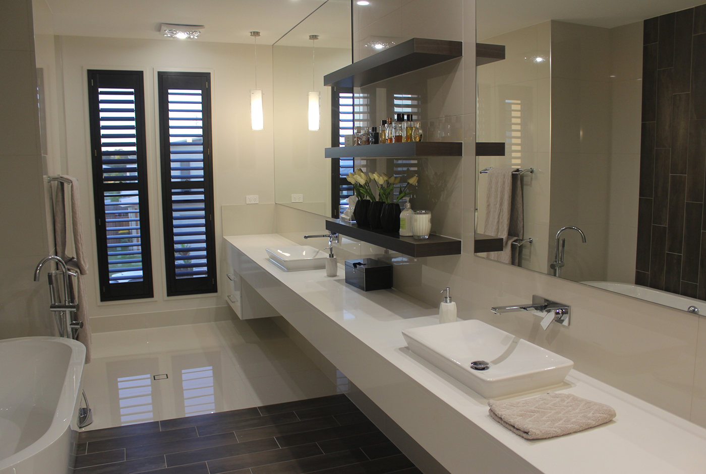 Master bathroom remodel featuring double sinks, a large mirror, wall-mounted shelves, a freestanding bathtub, and dark wood flooring.