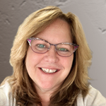 lmoriello2 A person with shoulder-length blonde hair and glasses, a smile reflecting the confidence of one of the best home inspectors, stands against a gray background.