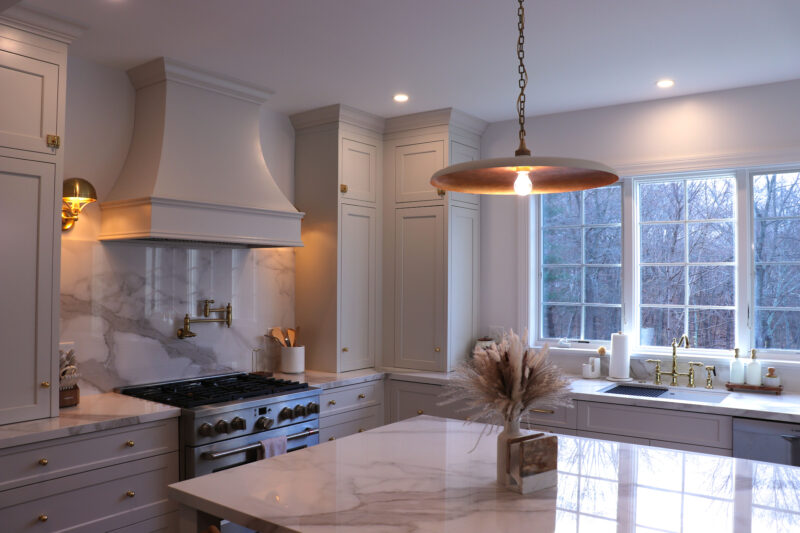 Modern kitchen with white cabinets, marble countertops, a central island, and a large window. A pendant light hangs over the island.