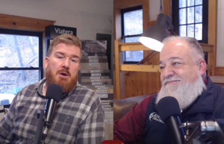 Two men engage in conversation during a recorded session in a room with wooden interior and a window in the background.