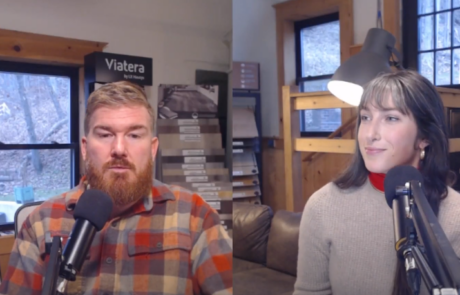 Two people sitting at a table with microphones in a room with shelves and a window, conducting a discussion or interview.