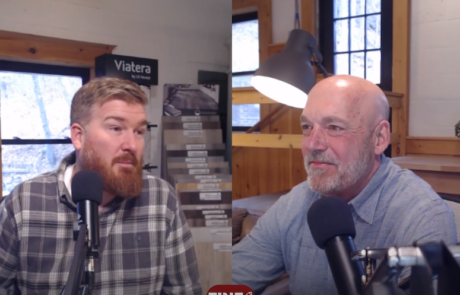 Two men seated indoors, speaking into microphones. Shelves in the background hold materials samples. A lamp and plant are also visible.