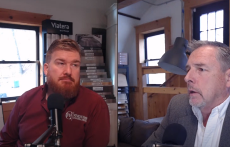 Two men sitting indoors having a conversation, each speaking into a microphone, with home improvement samples in the background.