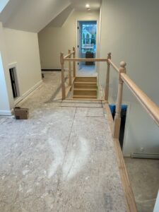 A partially constructed attic space with a wooden railing and staircase leading to a small door and window at the far end, ideal for a future kitchen remodel.