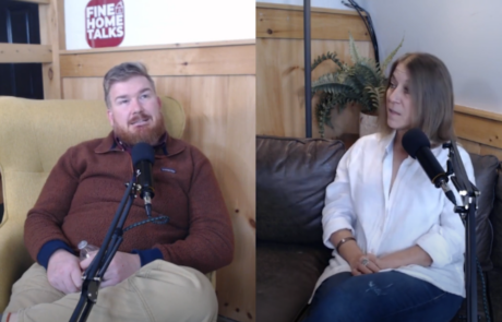 Two people sitting and talking on chairs with microphones, in a room with wooden walls and a plant in the background.