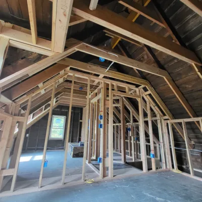 Wooden framing of a house under construction, showcasing exposed beams, studs, and electrical wiring against an unfinished interior.