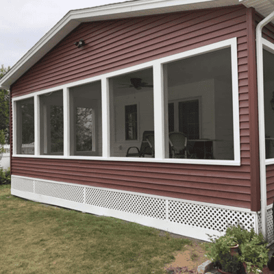 A red house with white trim features a screened-in porch with outdoor furniture, overlooking a lawn with a small garden in the corner.