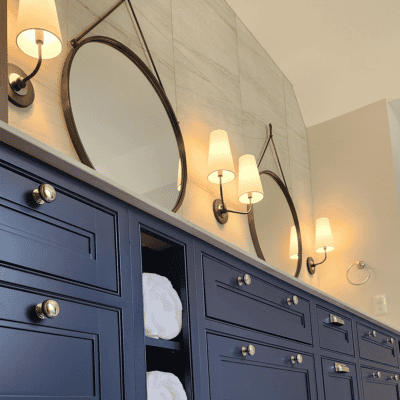 A bathroom vanity with dark blue cabinets, round mirrors, wall sconces, and towels stored in open shelves.