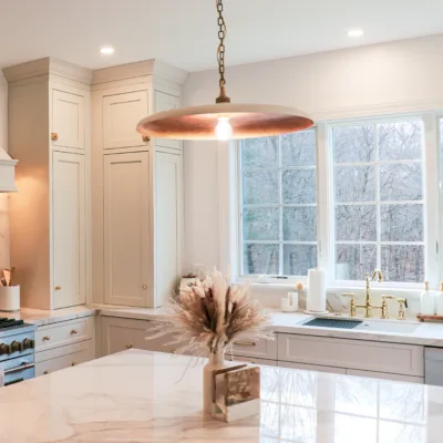 A modern kitchen with white cabinets, a marble countertop, a large window, and a decorative plant vase on the island.