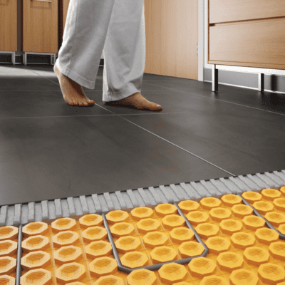 Person walking on tiled floor with visible underfloor heating system being installed beneath the tiles.