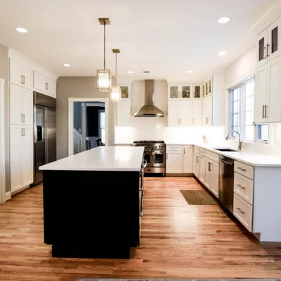 Modern kitchen with white cabinets, stainless steel appliances, an island with a white countertop, and wooden flooring.