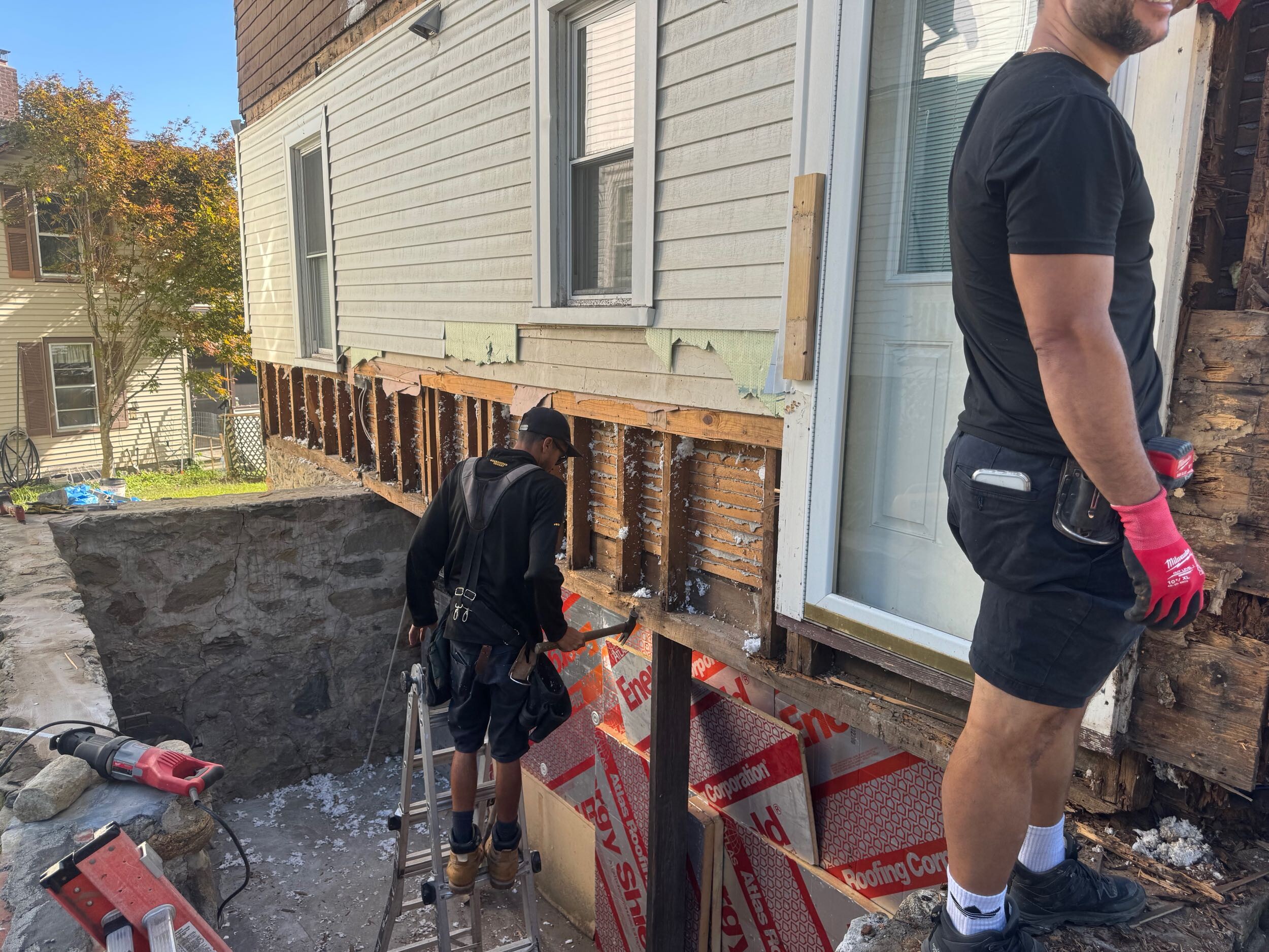 Carpenters repairing wall framing during a multi-level porch renovation